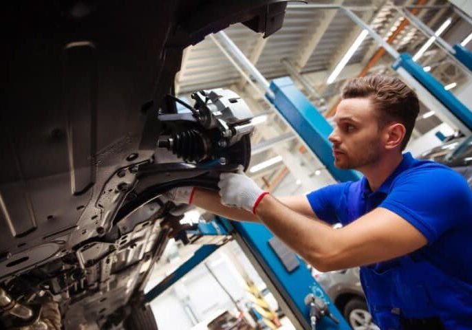 cheerful-handsome-confident-car-repair-specialist-overalls-repairs-replaces-old-parts-with-new-ones-car-lift-service
